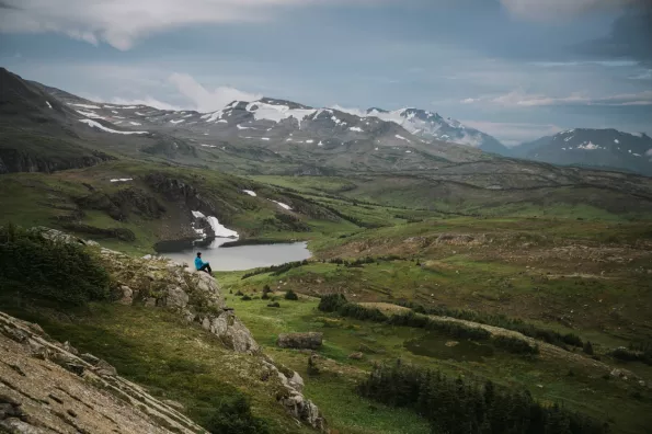 image of hiker overlooking a green field and mountains in the distance