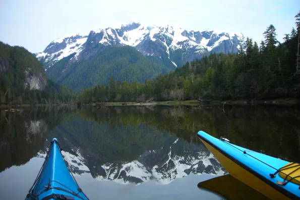 image of front of kayaks on a lake with mountain in distance reflecting on the clear water