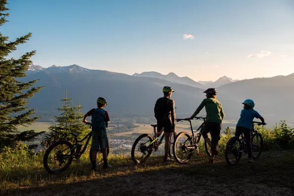 A family of four on bikes overlooking a valley below with mountains in the distance.