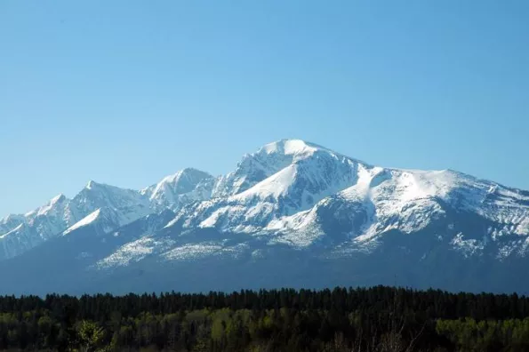 A mountain with trees below and a blue sky in the background