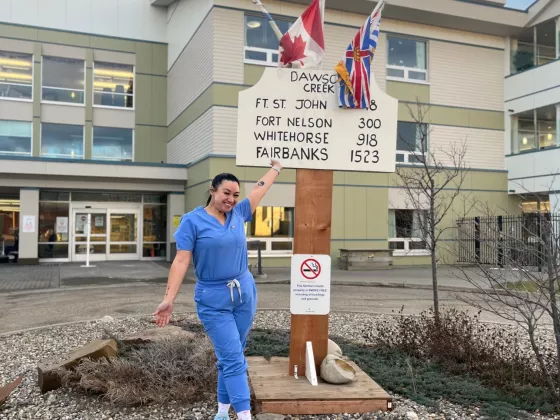Person standing in front of hospital with a sign with flags on it. 